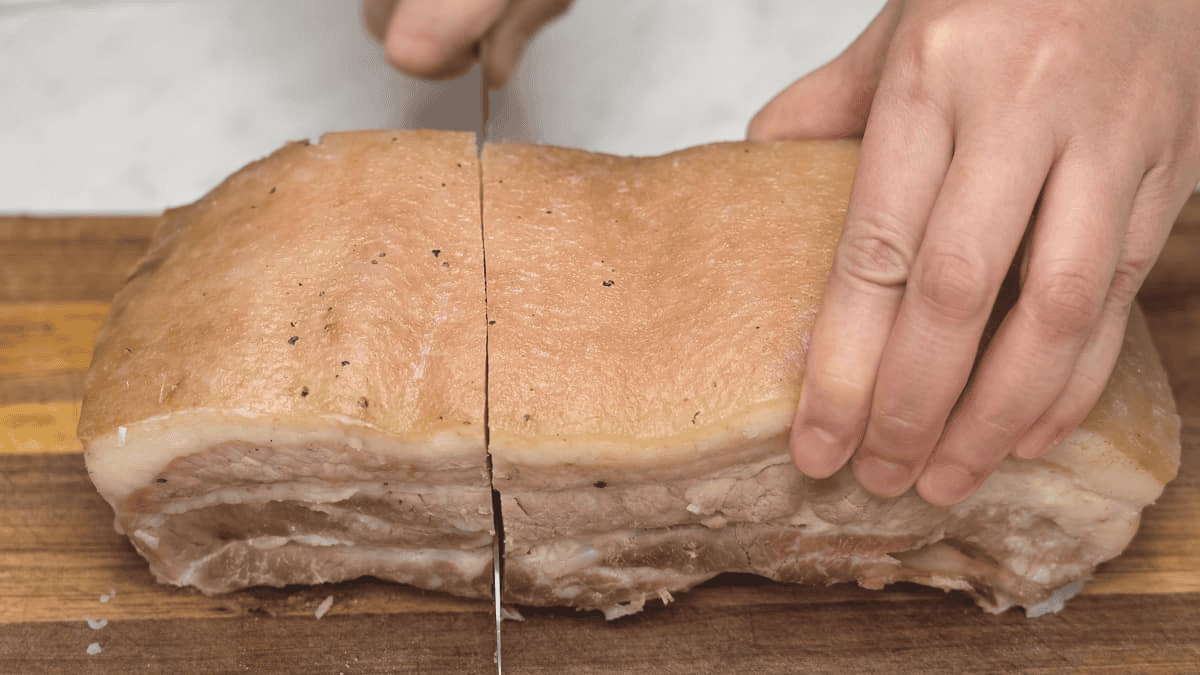 Slicing the pork belly slab on a cutting board.