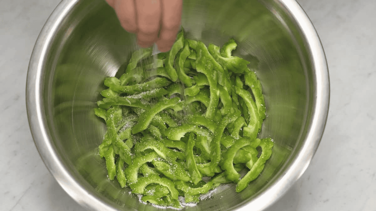 Adding salt to bitter melon slices in the bowl.