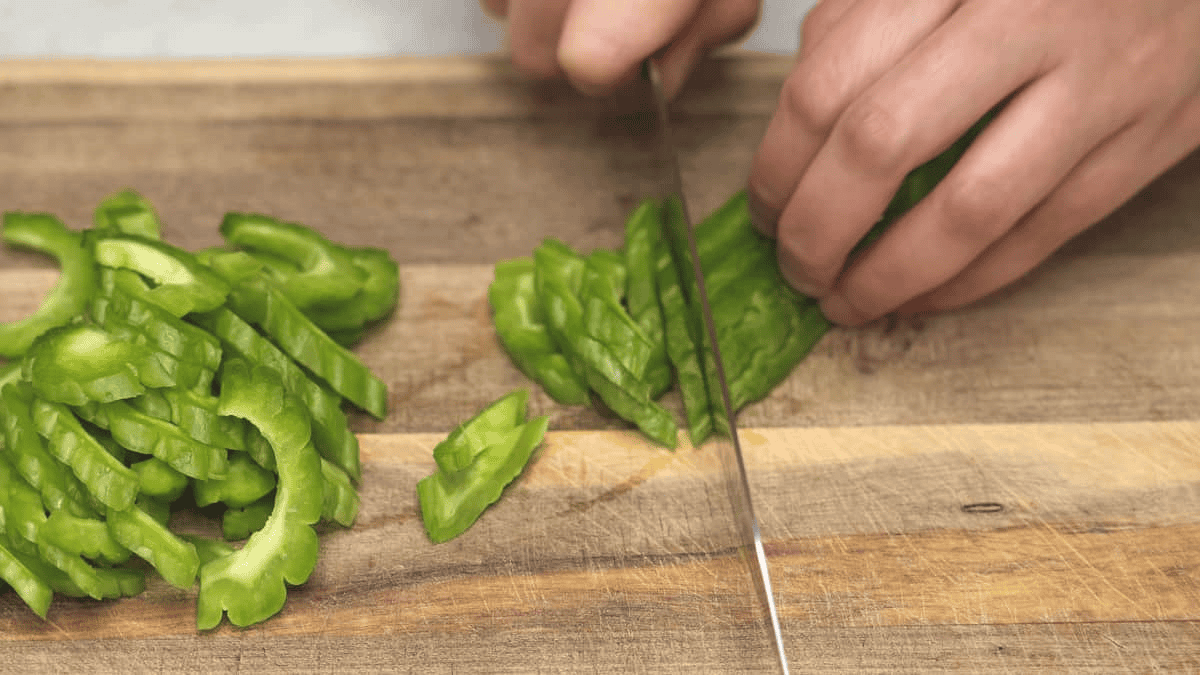 Slicing the bitter melon on a cutting board.