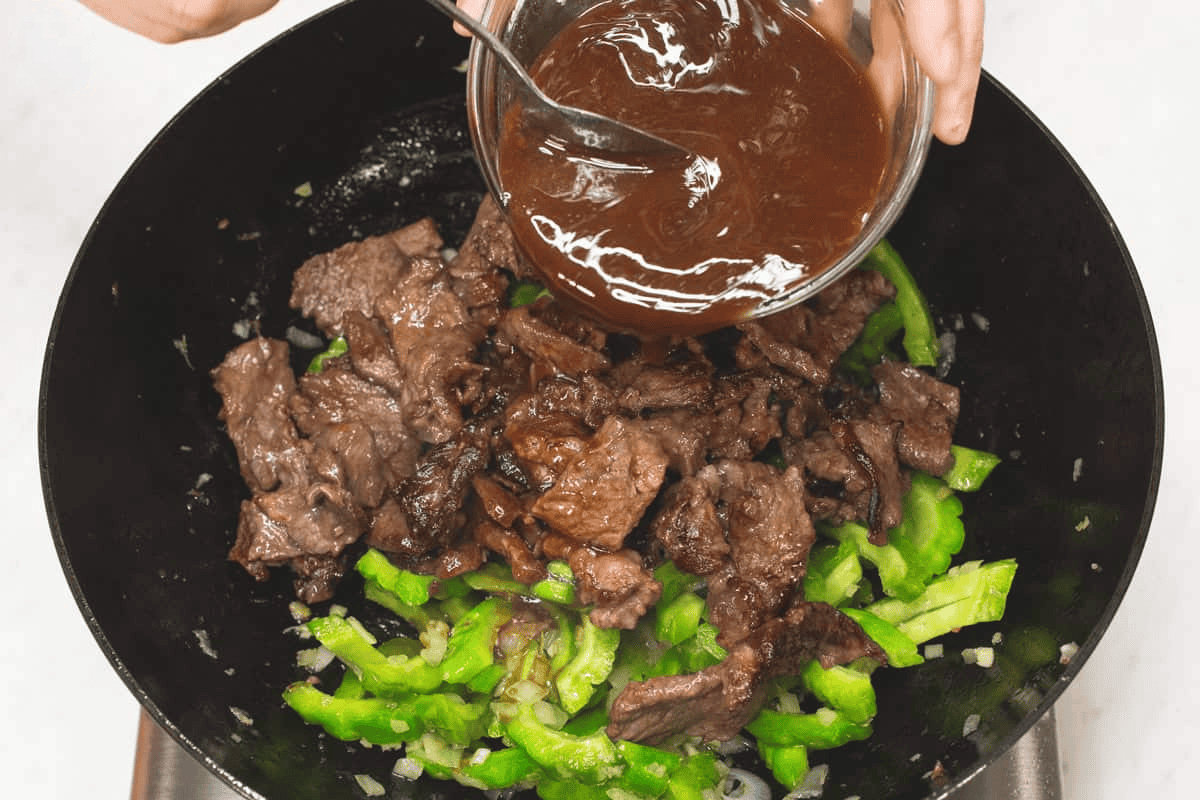 Adding the sauce to the ampalaya and beef in the wok.