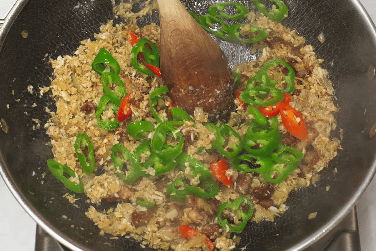 Added chili peppers to the shrimp paste and pork mixture in the wok.