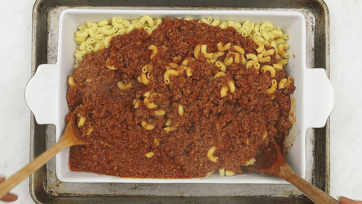 Mixing the macaroni and meat sauce in the casserole dish.