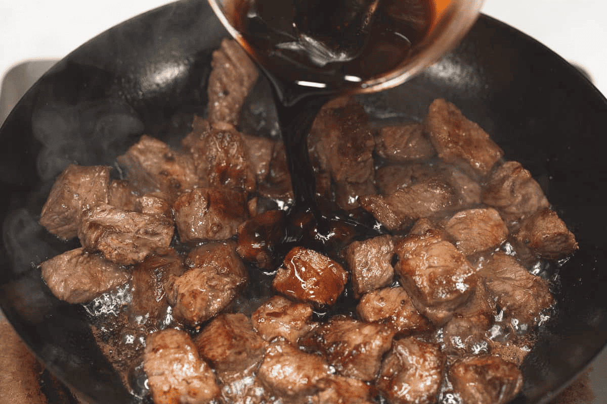 Adding the sauce to the seared beef in the wok.