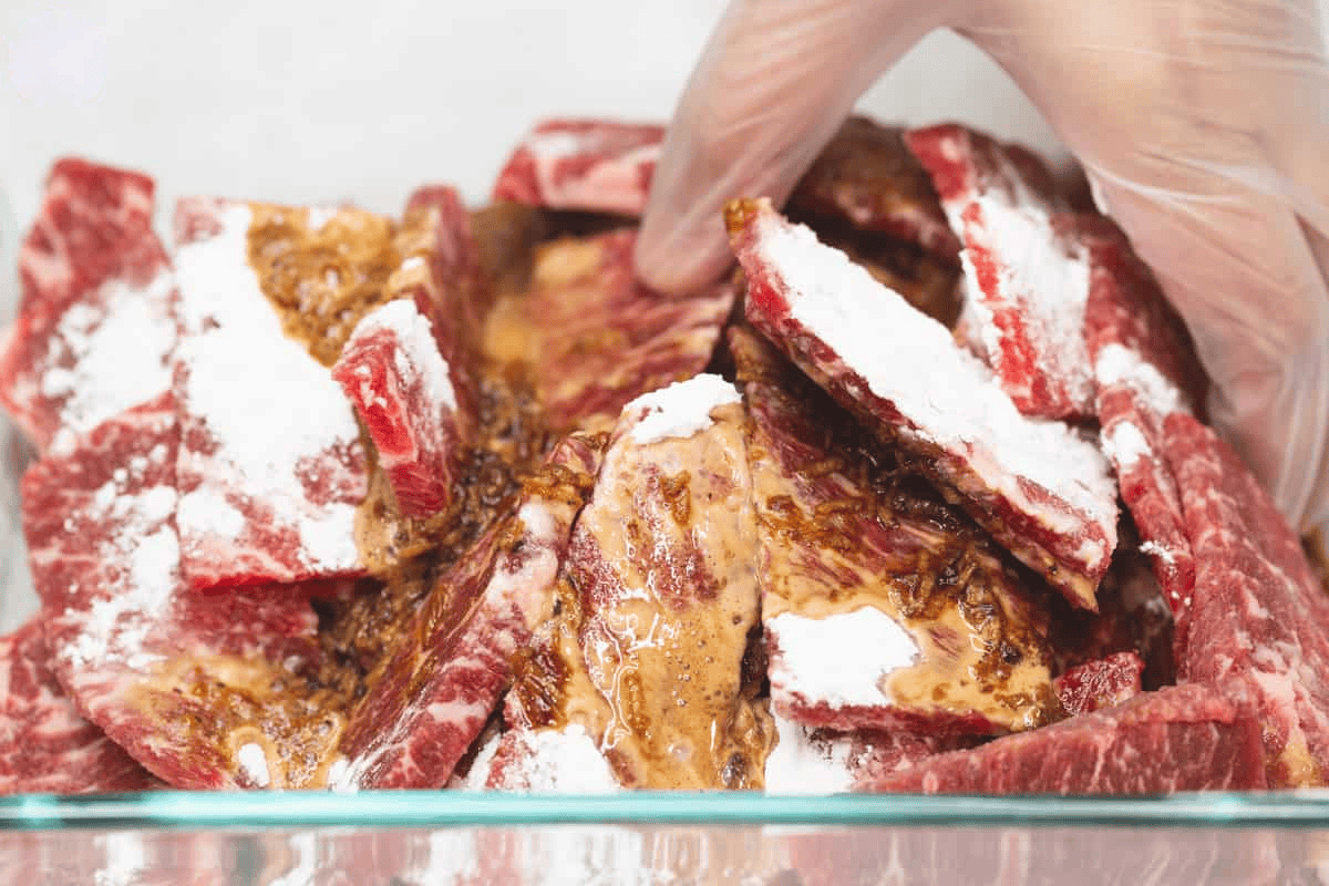 Marinating and velveting the beef with baking soda and cornstarch in a glass container.