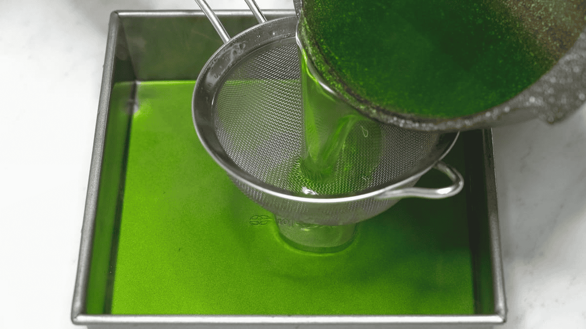 Straining agar-agar mixture through a fine-mesh sieve into a pan.