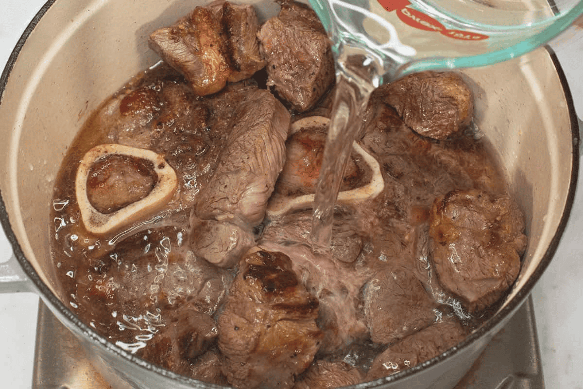 Adding the water to the meat in the pot.