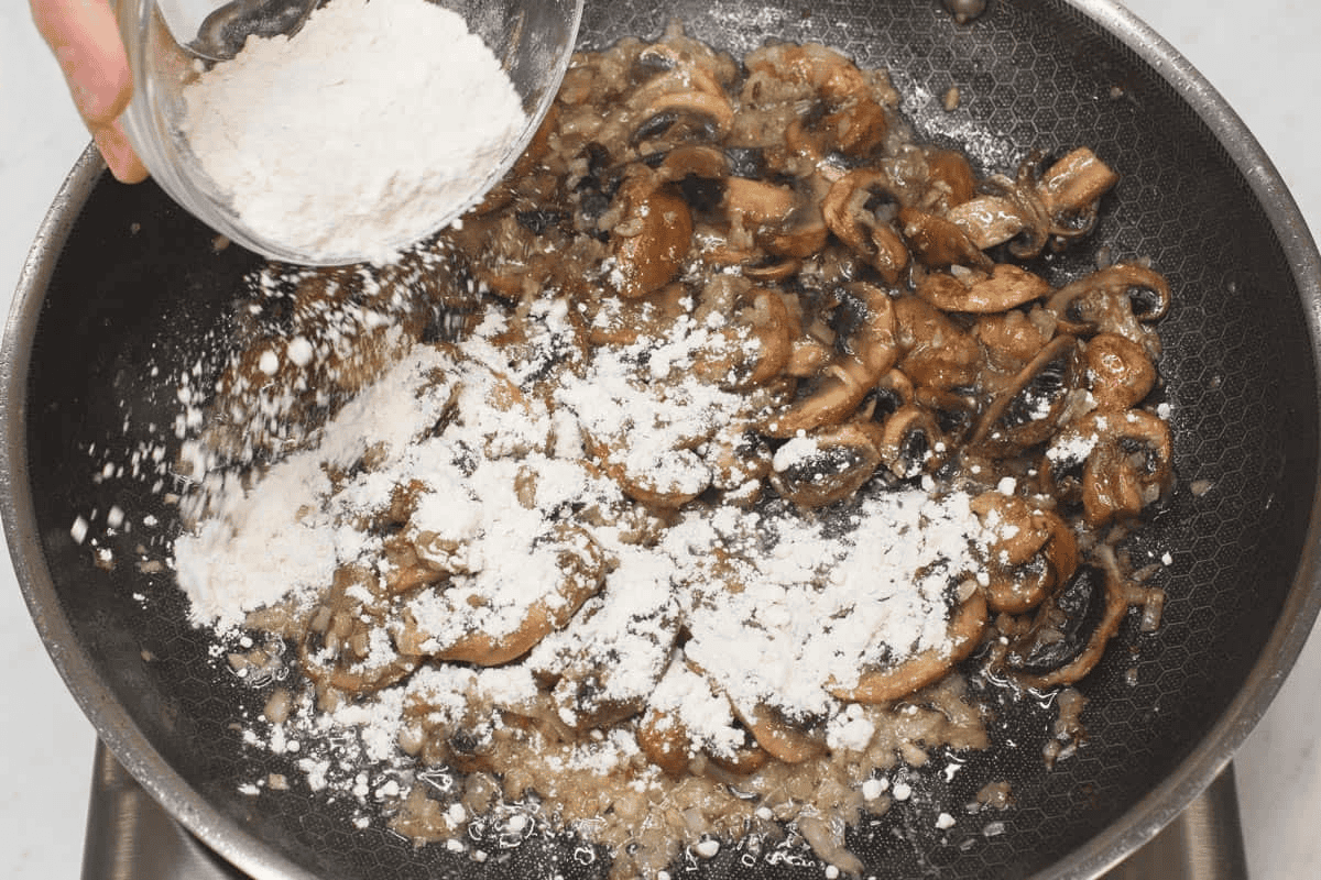 Sprinkling the flour to the mushrooms and aromatics in the skillet.