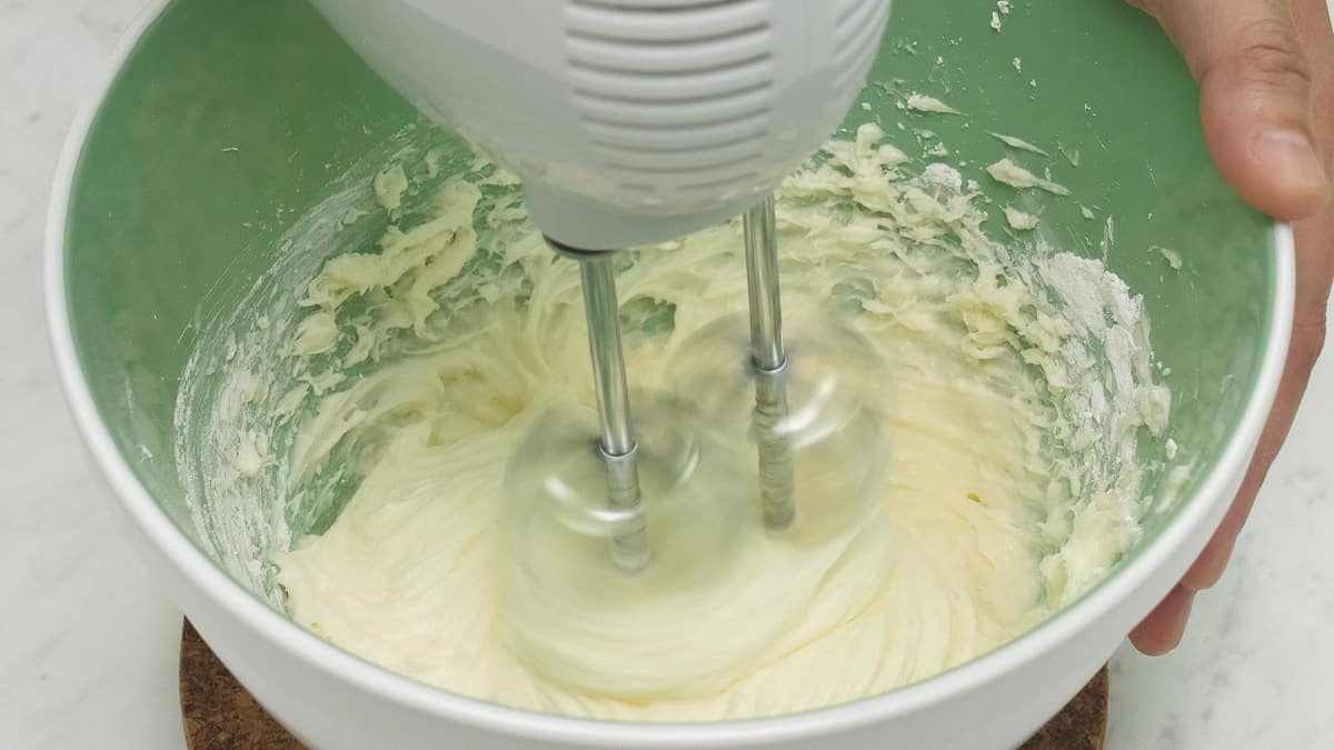 Mixing the cream cheese frosting using a hand mixer.