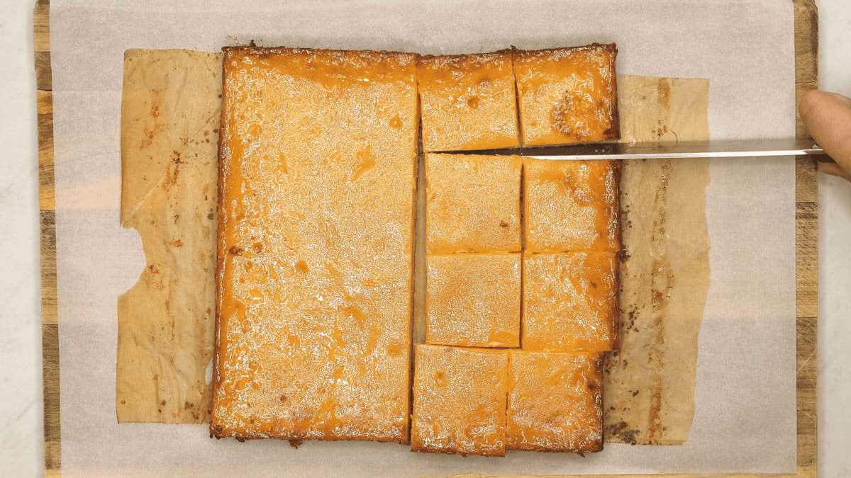 Cutting the cassava cake into squares with a knife.