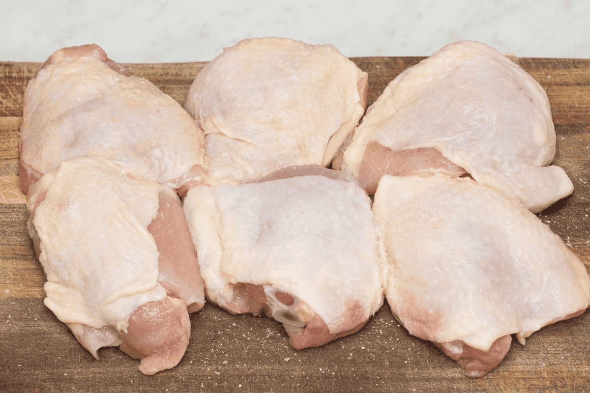 Chicken thighs season with salt on a cutting board.
