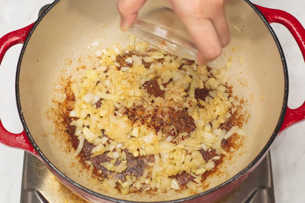 Adding crushed red pepper to the sauteed aromatics in the pot.