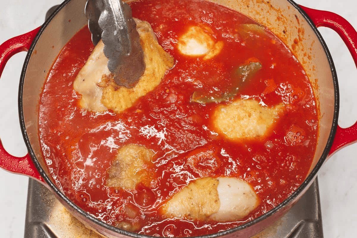Adding the chicken to the simmering sauce in the pot.