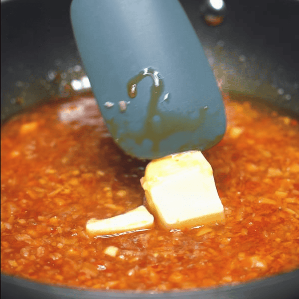 Adding butter to the sauce in a pan.