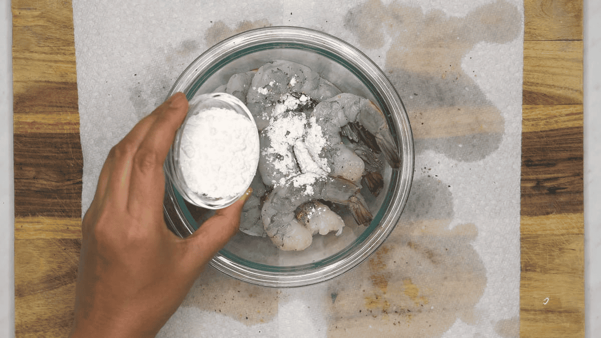 Adding cornstarch to the shrimp in the bowl.