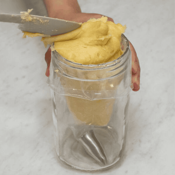 Filling a piping bag with churros dough using a tall glass.