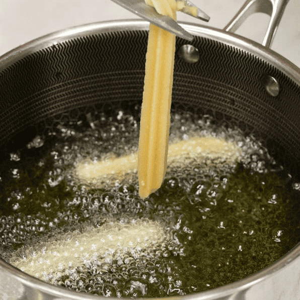 Piping churros dough into hot oil and cutting it with scissors.