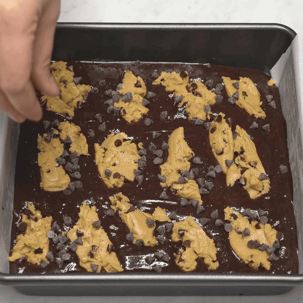 Adding chocolate chips to the unbaked brookie bars in the pan.