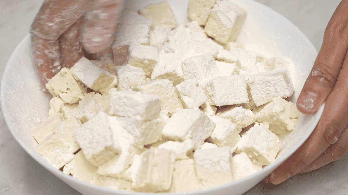 Coating the tofu cubes with starch in a bowl.