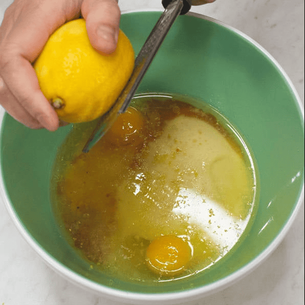 Zesting a lemon over the wet ingredients in a bowl.