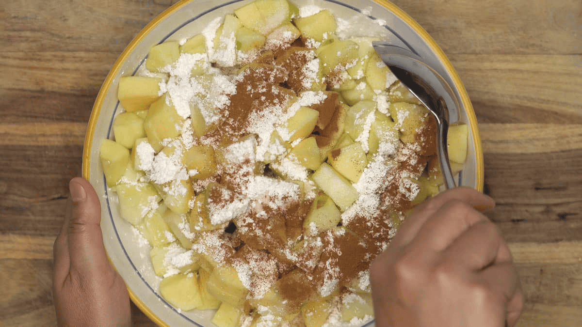 Mixing the apples with sugar, cornstarch, and cinnamon in the bowl with a spoon.