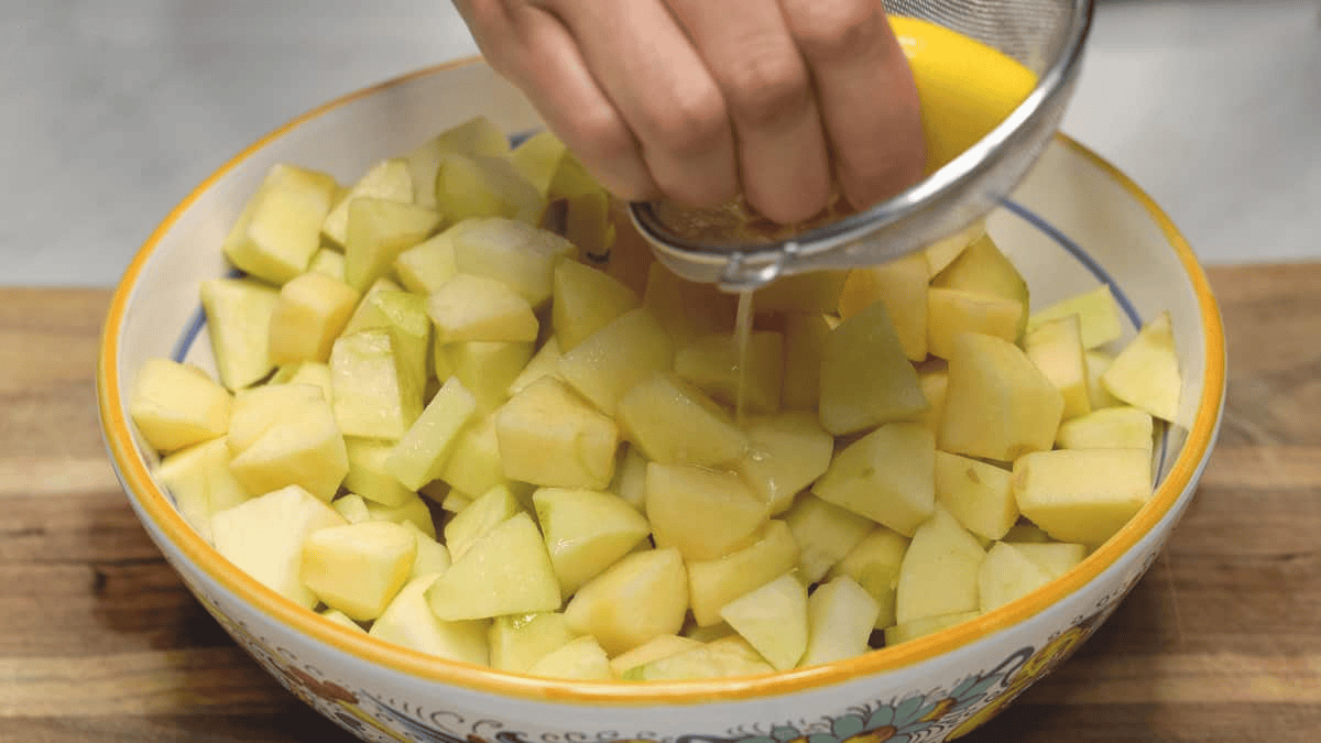 Squeezing a half of lemon over the apples in the bowl while straining the seeds with a sieve. 