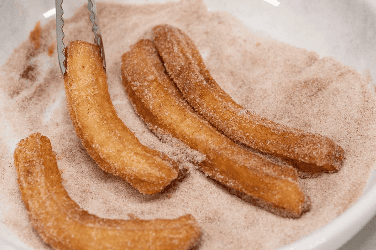 Coating the churros with cinnamon sugar.