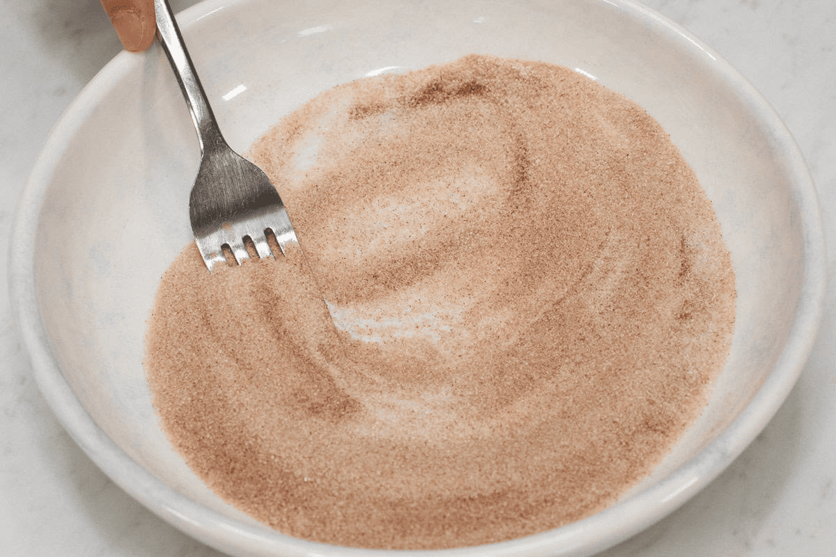 Mixing cinnamon powder and sugar in a shallow bowl.