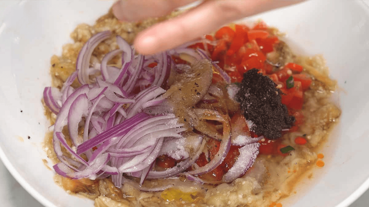Adding pepper to the eggplant salad in the bowl.