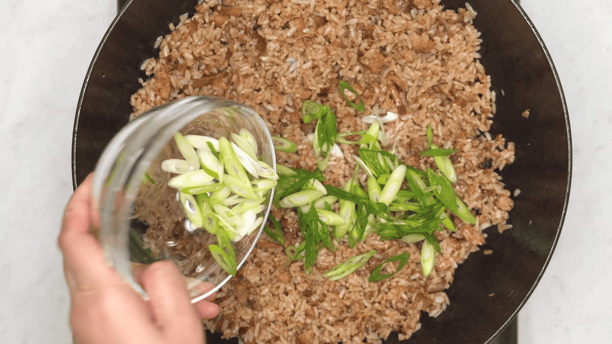 Adding scallions to the adobo fried rice in the wok.
