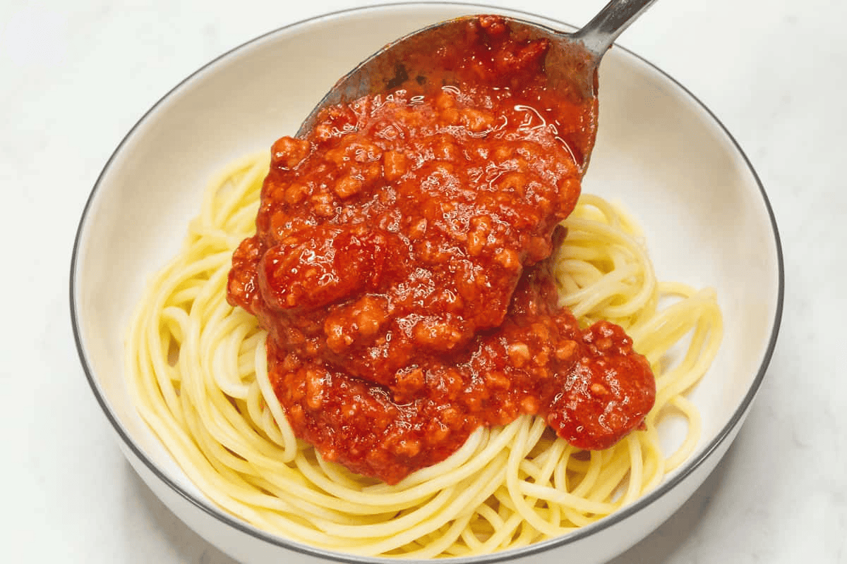 Pouring the meat sauce over the spaghetti in the bowl.