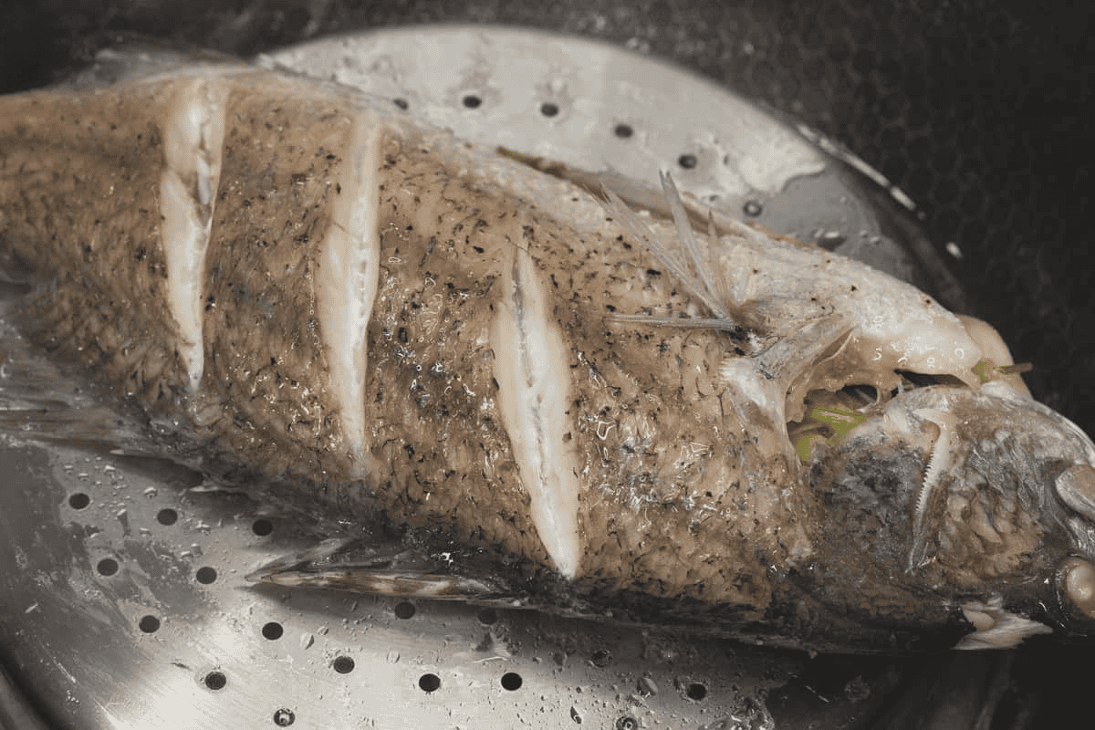 Steamed fish on an inverted steamer basket in a wok.