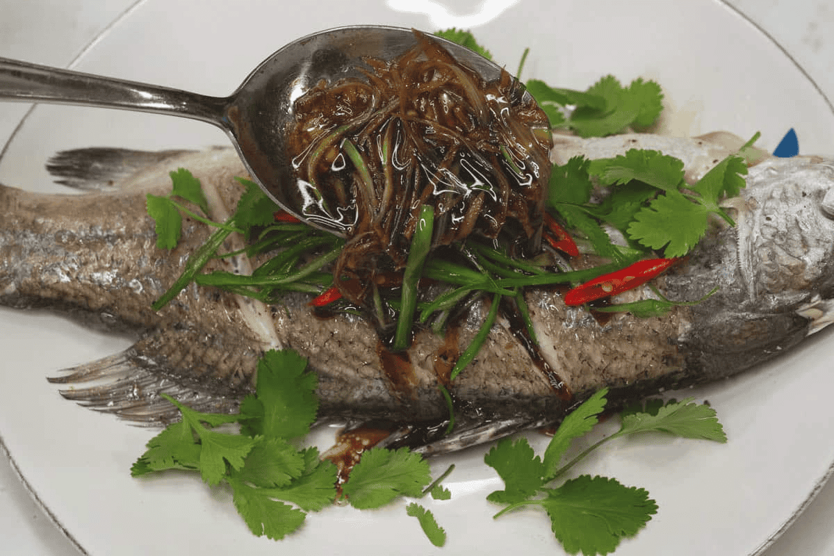 Pouring the sauce over the fish with garnishes.