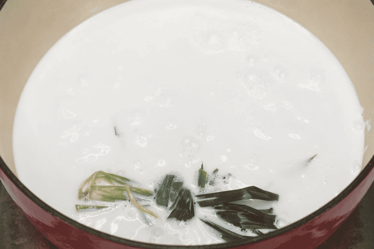 Boiling coconut milk and pandan leaves in a pot.