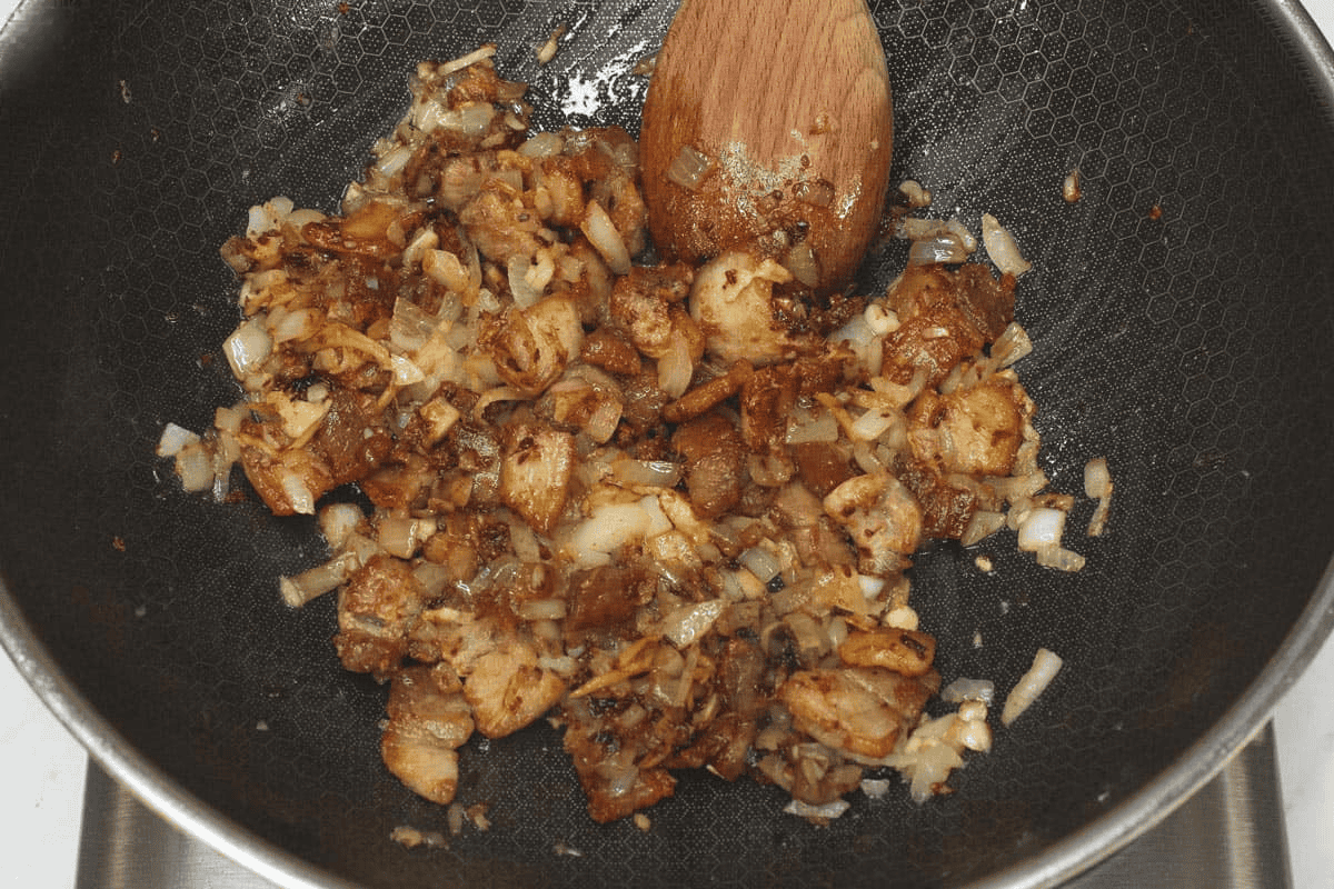 Sauteing pork and aromatics with shrimp paste in a wok.