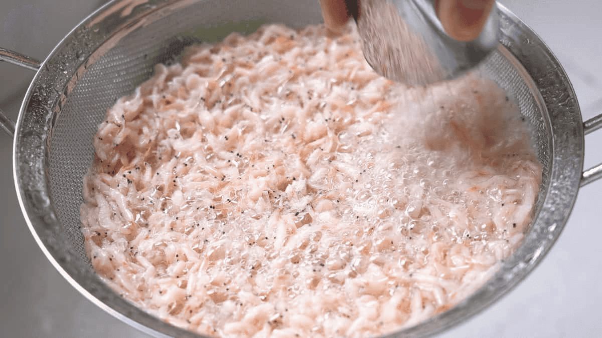 Rinsing the shrimp paste using a strainer or a fine mesh sieve.