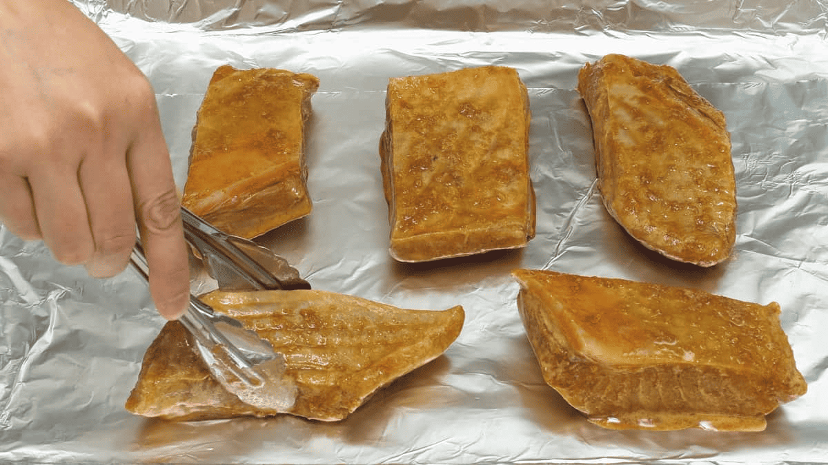 Arranging the marinated tuna belly slices on the aluminum foli-lined baking sheet.