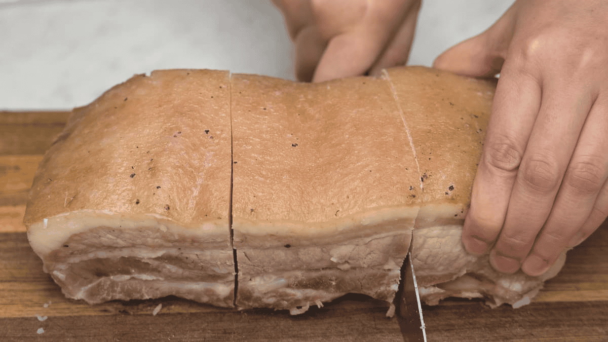 Cutting the cooked slab of pork belly into smaller pieces.