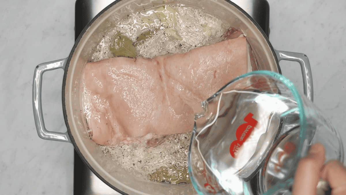 Adding water to the slab of pork belly in the pot.
