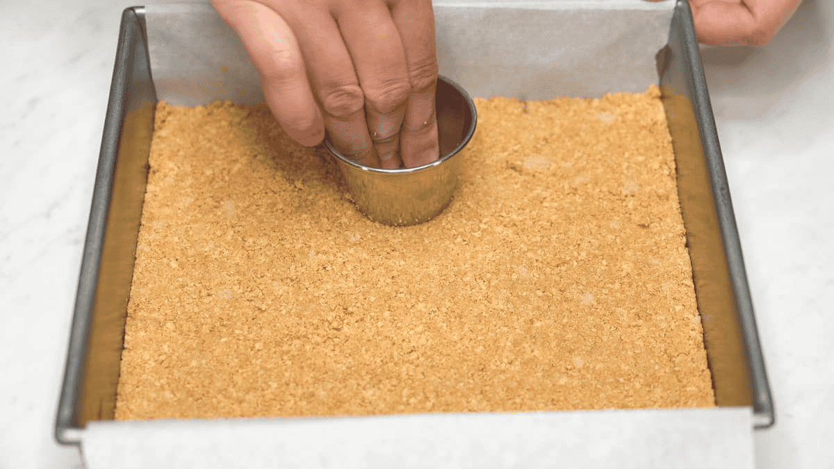 Pressing down the graham crust into the pan using a ramekin.