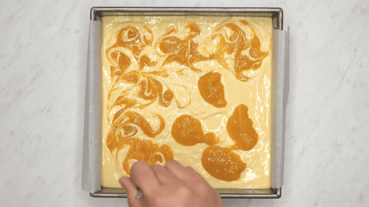 Swirling the dollops of mango puree on top of the cheesecake batter.