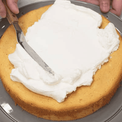 Spreading whipped cream on the first mango cake layer.