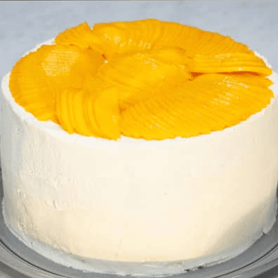 Mango chiffon cake covered with frosting and topped with sliced mangoes.