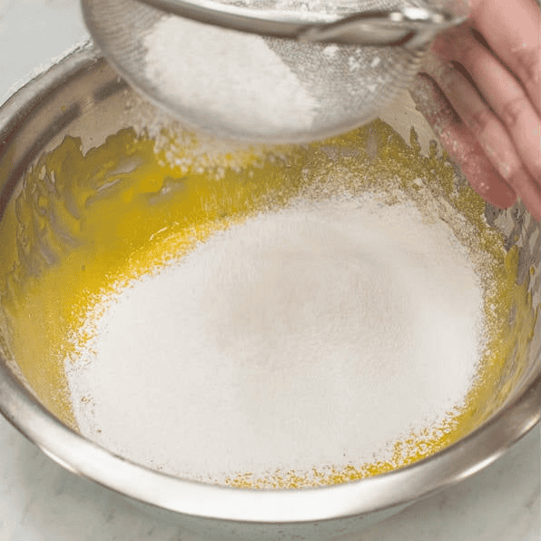 Sifting dry ingredients into the mango cake batter.