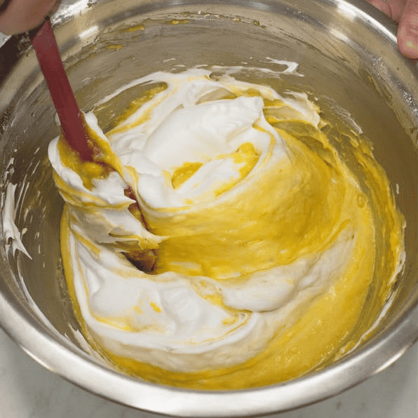Folding white meringue into the yellow mango batter.