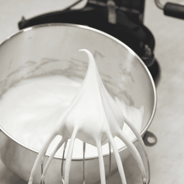 Whipped meringue holding firm peaks on the whisk.