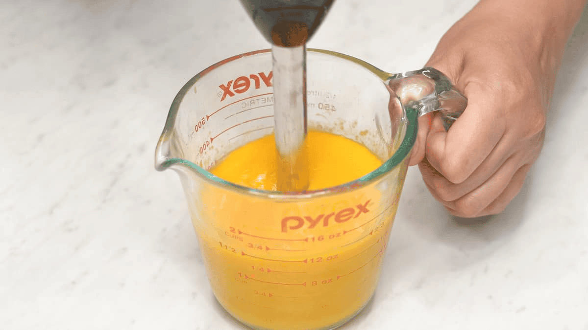 Blending the mangoes in the cup using an immersion blender.