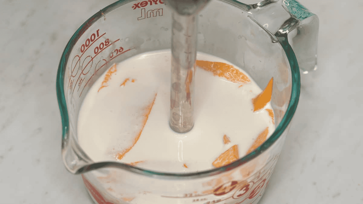 Blending half and half, condensed milk, and mangoes with an immersion blender.