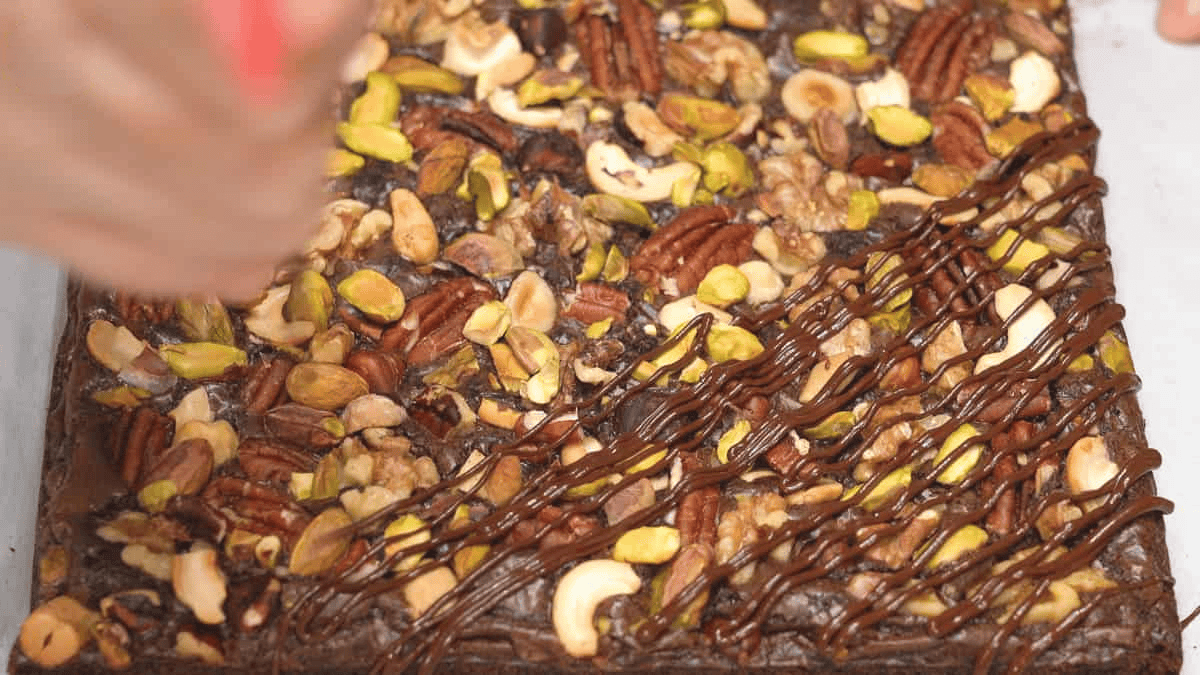 Drizzling chocolate on the brownies with nuts.