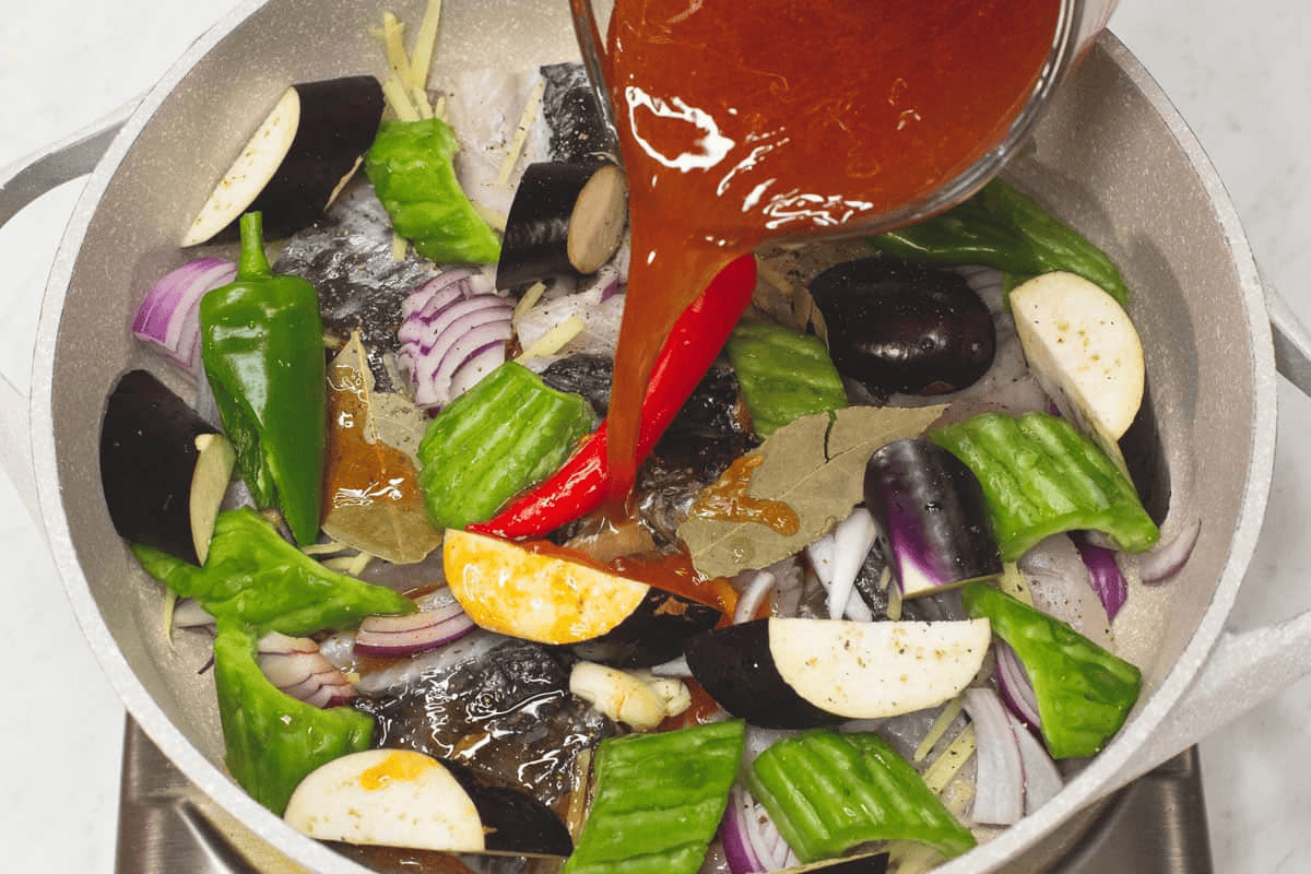 Pouring the sauce over the bangus and other ingredients in the pan.