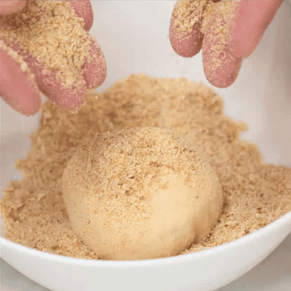 Coating a dough ball with breadcrumbs.